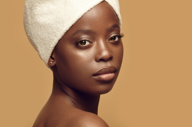 Afro-Amerikaanse vrouw met een gezonde en schone huid, gekleed in een spa-hoofddoek op een beige achtergrond