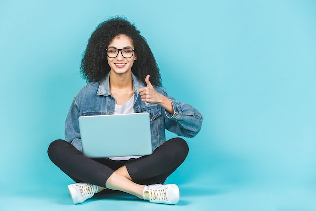 Afro-amerikaanse vrouw met laptop zittend op een vloer met gekruiste benen