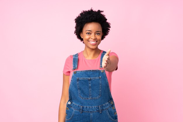 Afro-Amerikaanse vrouw met onalls op geïsoleerde roze handshaking na goede deal