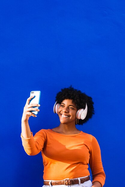 Afro-Amerikaanse vrouw met oranje trui en witte koptelefoon die een mobiel neemt