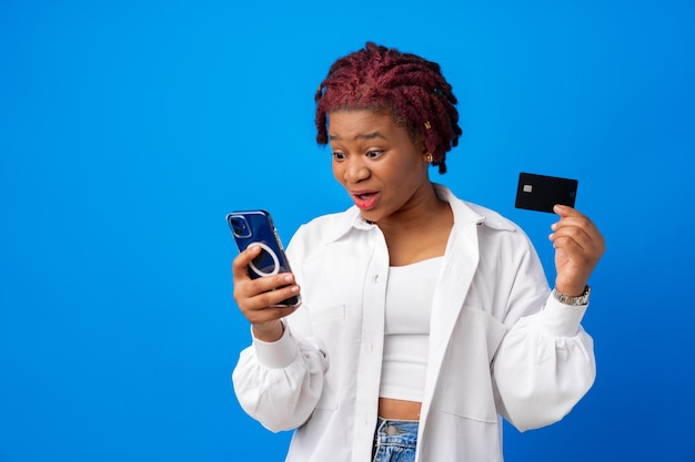 Afro-Amerikaanse vrouw met smartphone en creditcard tegen blauwe achtergrond