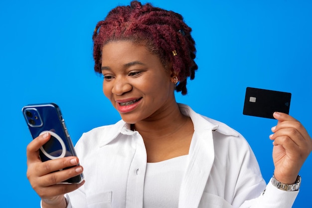 Afro-Amerikaanse vrouw met smartphone en creditcard tegen blauwe achtergrond