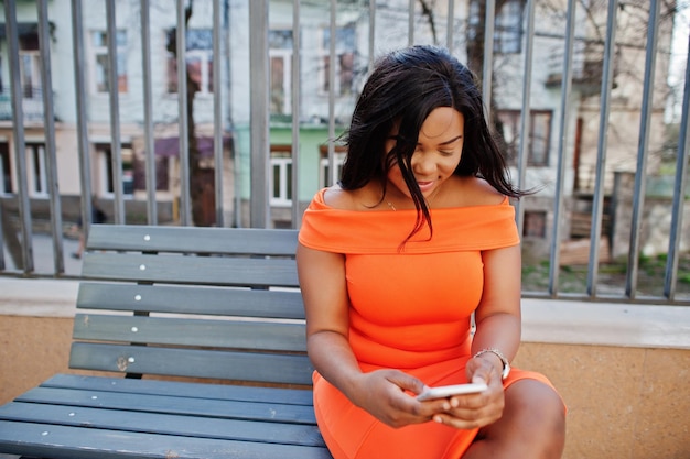 Afro-amerikaanse vrouw model xxl in oranje jurk op zoek op mobiele telefoon