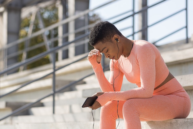 Afro-Amerikaanse vrouw moe na training luisteren naar muziek en audio podcast, na joggen en trainen in het stadion in de ochtend