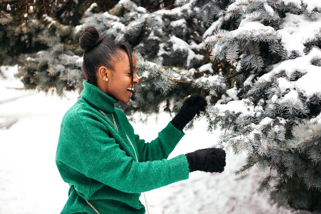 Afro-amerikaanse vrouw staat buiten op straat in de buurt van de kerstboom en speelt witte sneeuw die naar beneden valt?