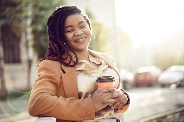 Afro-amerikaanse vrouw staat in een srteet met afhaalmaaltijden koffiekopje