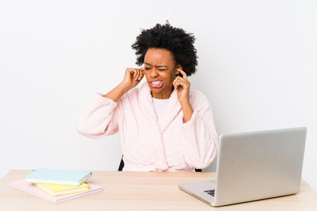 Afro-Amerikaanse vrouw van middelbare leeftijd die geïsoleerd thuis werken behandelt oren met handen.