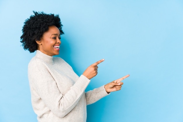 Afro-amerikaanse vrouw van middelbare leeftijd tegen een blauwe geïsoleerde opgewonden wijzend met wijsvingers weg.