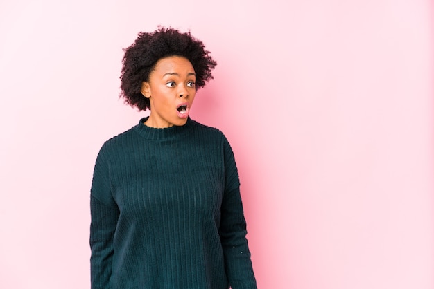Afro-Amerikaanse vrouw van middelbare leeftijd tegen een roze geïsoleerd wordt geschokt vanwege iets dat ze heeft gezien.