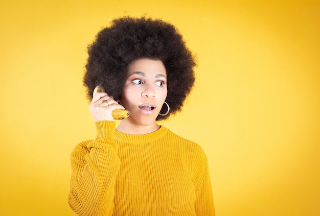 Afro-Amerikaanse vrouw wsing een banaan als een telefoon op gele achtergrond