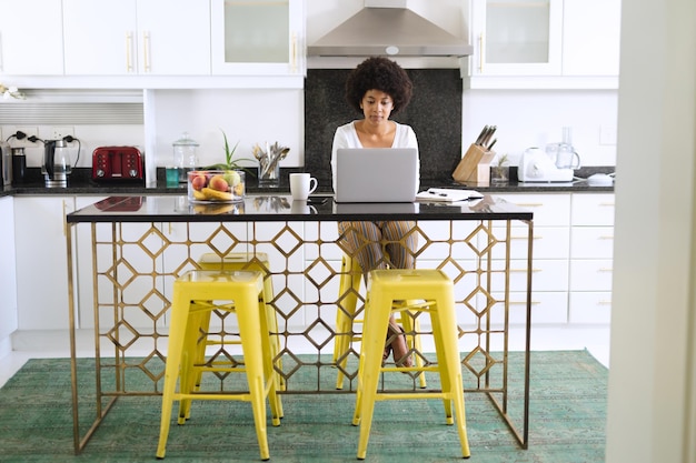 Afro-Amerikaanse vrouw zit in de keuken met behulp van laptop