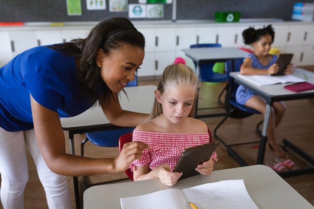 Foto afro-amerikaanse vrouwelijke leraar die een meisje leert om digitale tablet te gebruiken in de klas op de basisschool