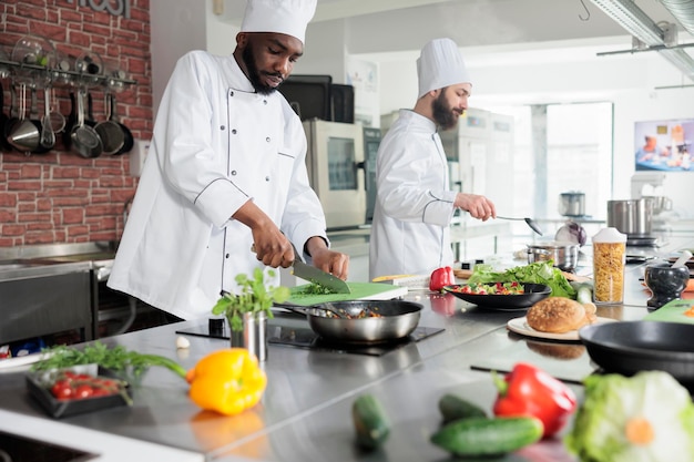 Afro-Amerikaanse werknemer in de voedingsindustrie die verse biologische kruiden hakt terwijl hij een gastronomisch gerecht kookt Chef-kok in voorbereidingsproces van diner in de professionele keuken van het restaurant.