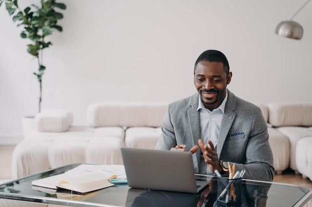 Afro-Amerikaanse zakenman communiceert met klant via videogesprek zittend aan bureau met laptop