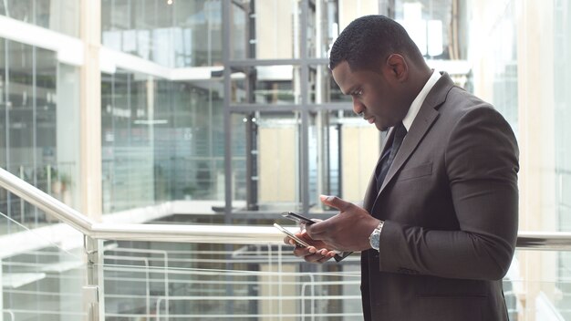 Afro-Amerikaanse zakenman die e-mails op zijn smartphone leest en antwoorden sms't