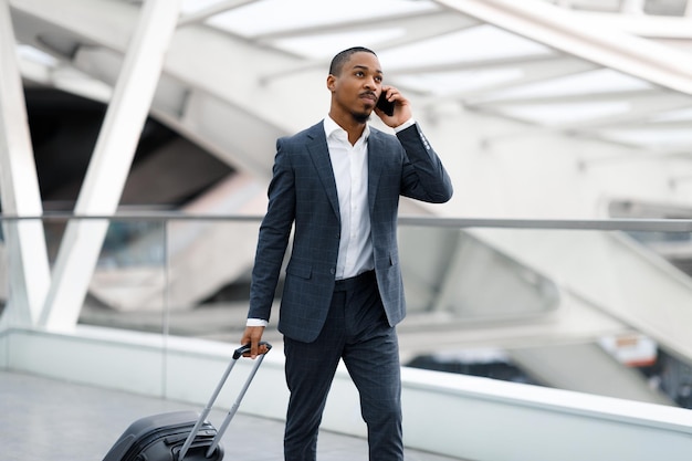 Afro-Amerikaanse zakenman die op mobiel praat terwijl hij met bagage op de luchthaven loopt