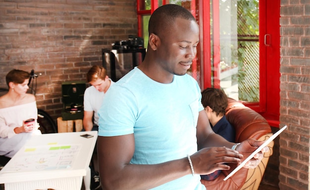 Afro-Amerikaanse zakenman gebruikt een digitale tablet en glimlacht terwijl hij in zijn kantoor zit