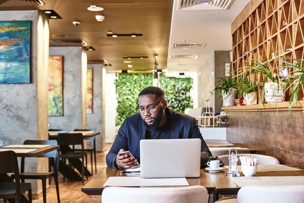 Afro-Amerikaanse zakenman werkt met zijn laptop terwijl hij uitrust in het café