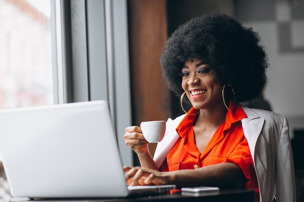 Afro-Amerikaanse zakenvrouw in wit pak die op laptop in een café werkt