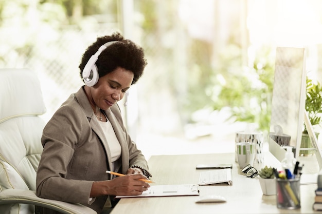 Afro-amerikaanse zakenvrouw met koptelefoon aan het werk terwijl ze alleen op het werk in een kantoor zit.