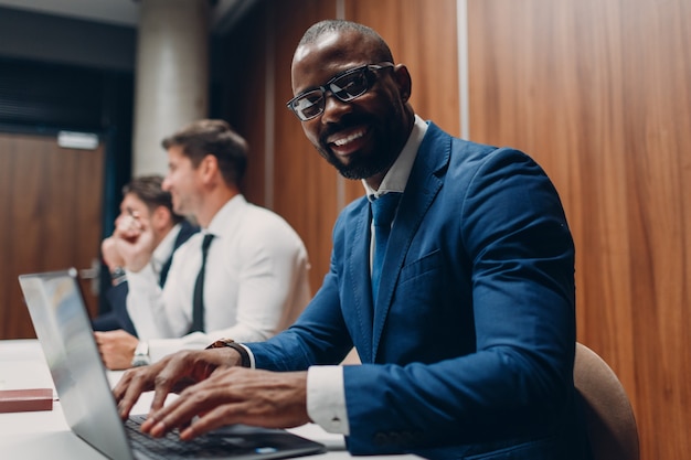 Afro-amerikaanse zwarte man zakenman zittend aan tafel met laptop op office team mensen achtergrond.