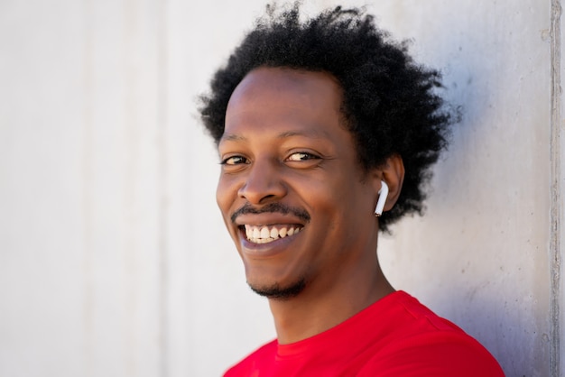 Photo afro athletic man wearing ear pods and smiling against the wall