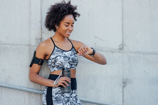 Afro athletic woman checking time on her smart watch while work out outdoors.