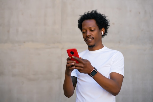 Afro atletische man met behulp van zijn mobiele telefoon en ontspannen na de training buitenshuis.