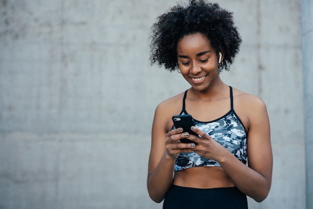 Afro atletische vrouw met behulp van haar mobiele telefoon en ontspannen na de training buitenshuis. Sport en technologie concept.