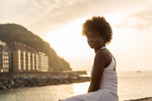 Afro beauty woman turning to look at camera while gazing the ocean during sunset