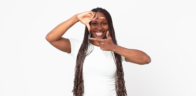 Afro black adult woman feeling happy, friendly and positive, smiling and making a portrait or photo frame with hands