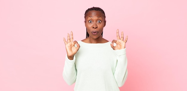 Afro black adult woman feeling shocked, amazed and surprised, showing approval making okay sign with both hands