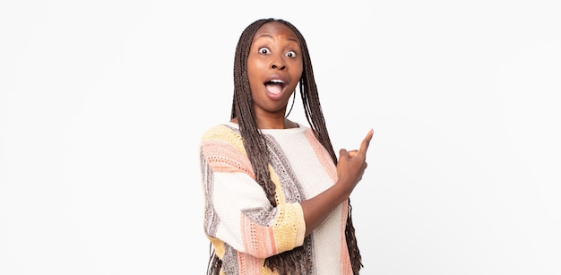 Afro black adult woman looking excited and surprised pointing to the side and upwards to copy space