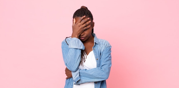 Afro black adult woman looking stressed, ashamed or upset, with a headache, covering face with hand