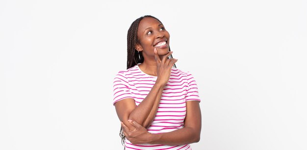 아프리카 흑인 성인 여성이 행복하게 웃고 공상을 하거나 의심하며 옆을 바라보고 있습니다.