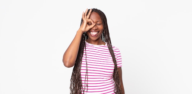 Afro black adult woman smiling happily with funny face, joking and looking through peephole, spying on secrets