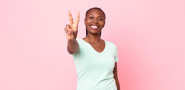 Afro black adult woman smiling and looking happy, carefree and positive, gesturing victory or peace with one hand