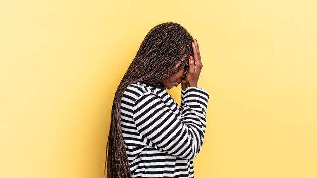 Afro black pretty woman covering eyes with hands with a sad, frustrated look of despair, crying, side view