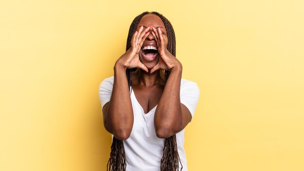 Bella donna afro nera che si sente felice, eccitata e positiva, dando un grande grido con le mani vicino alla bocca, chiamando