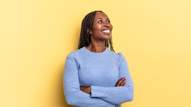 Afro black pretty woman feeling happy, proud and hopeful, wondering or thinking, looking up to copy space with crossed arms