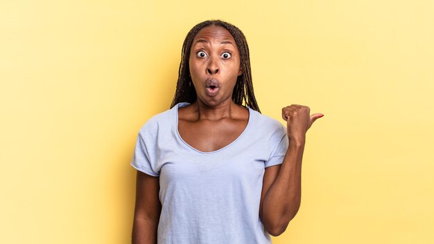 Afro black pretty woman looking astonished in disbelief, pointing at object on the side and saying wow, unbelievable