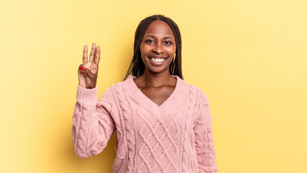 Afro black pretty woman smiling and looking friendly, showing number three or third with hand forward, counting down