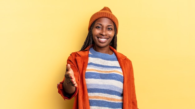 Afro black pretty woman smiling, looking happy, confident and friendly, offering a handshake to close a deal, cooperating