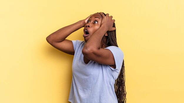 Afro black pretty woman with open mouth, looking horrified and shocked because of a terrible mistake, raising hands to head