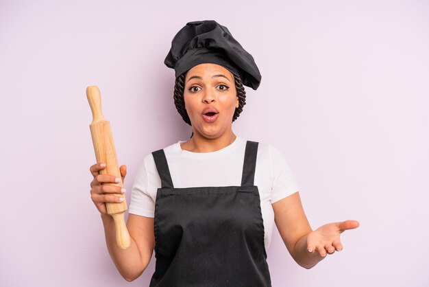 Afro black woman feeling extremely shocked and surprised. chef with a roller pin