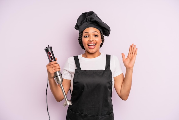 Afro black woman feeling happy and astonished at something unbelievable. chef with hand blender