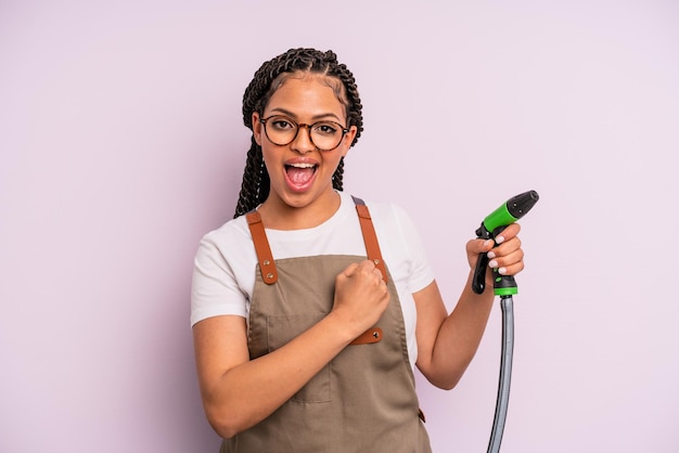 afro black woman feeling happy and facing a challenge or celebrating. gardener hose concept