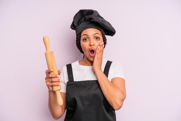 afro black woman feeling shocked and scared. chef with a roller pin