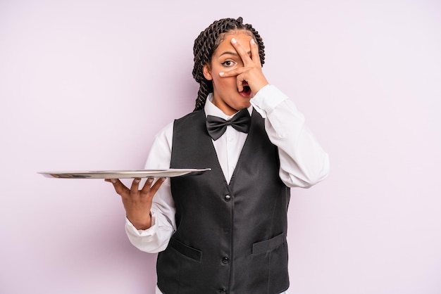 Afro black woman looking shocked scared or terrified covering face with hand waiter with a tray