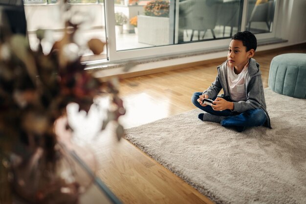 Afro boy sitting on the floor in the living room and playing video games